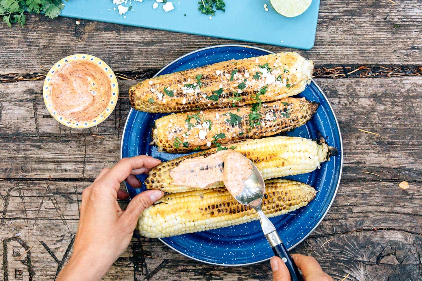 plaste of grilled mexican corn on the cob being smeared with dressing