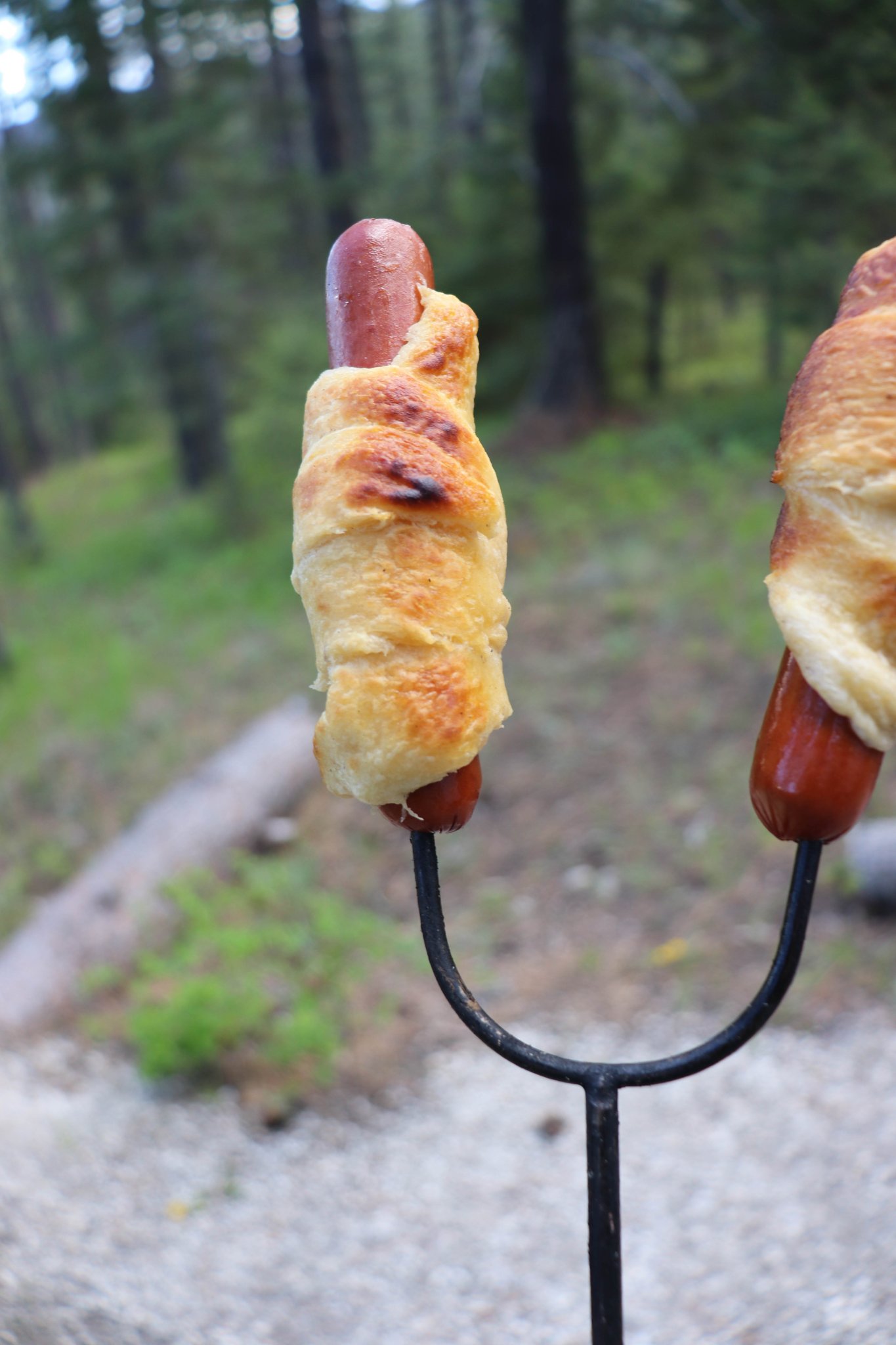 cooked hotdog wrapped in a crescent roll on a campfire skewer