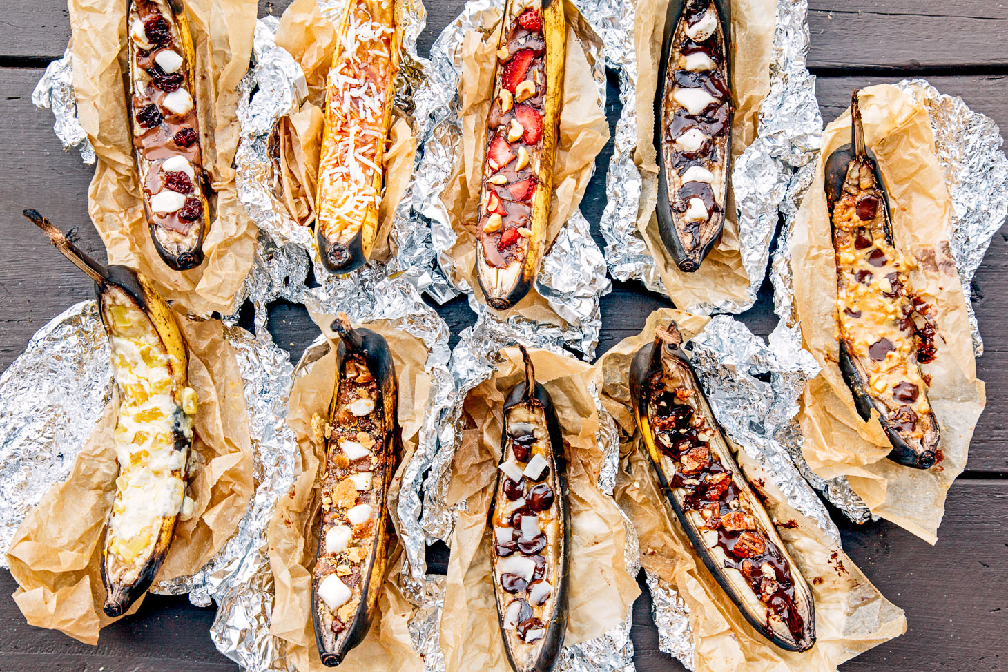 a platter of grilled bananas inside tin foil topped with strawberries and chocolate