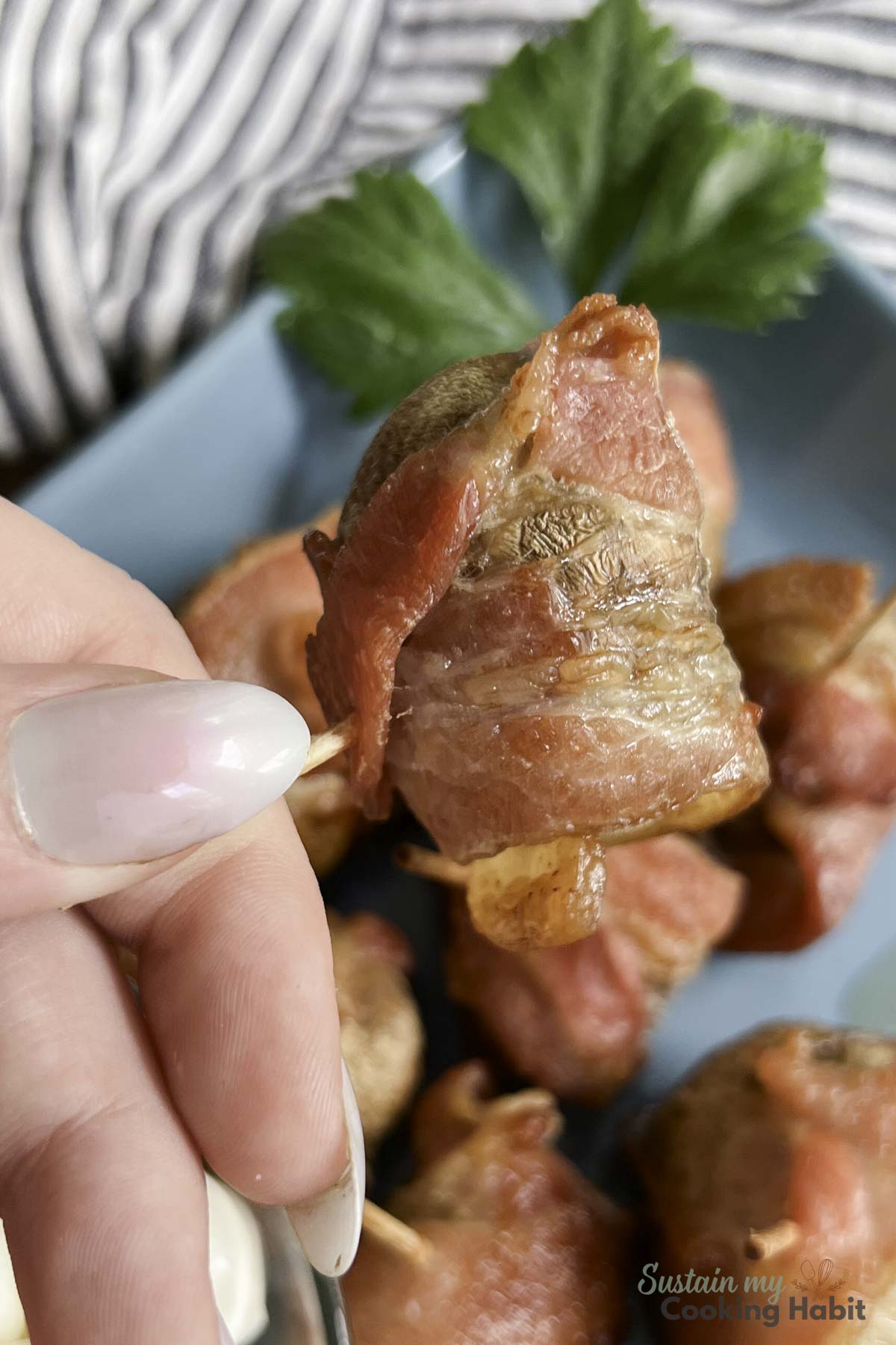 Hand holding a cooked bacon wrapped mushroom appetizer.
